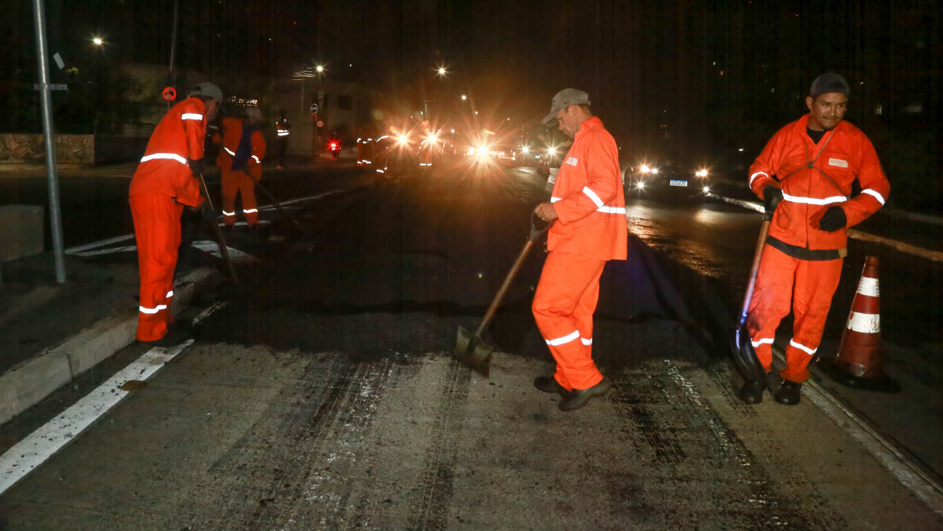 homens colocando asfalto em uma avenida à noite